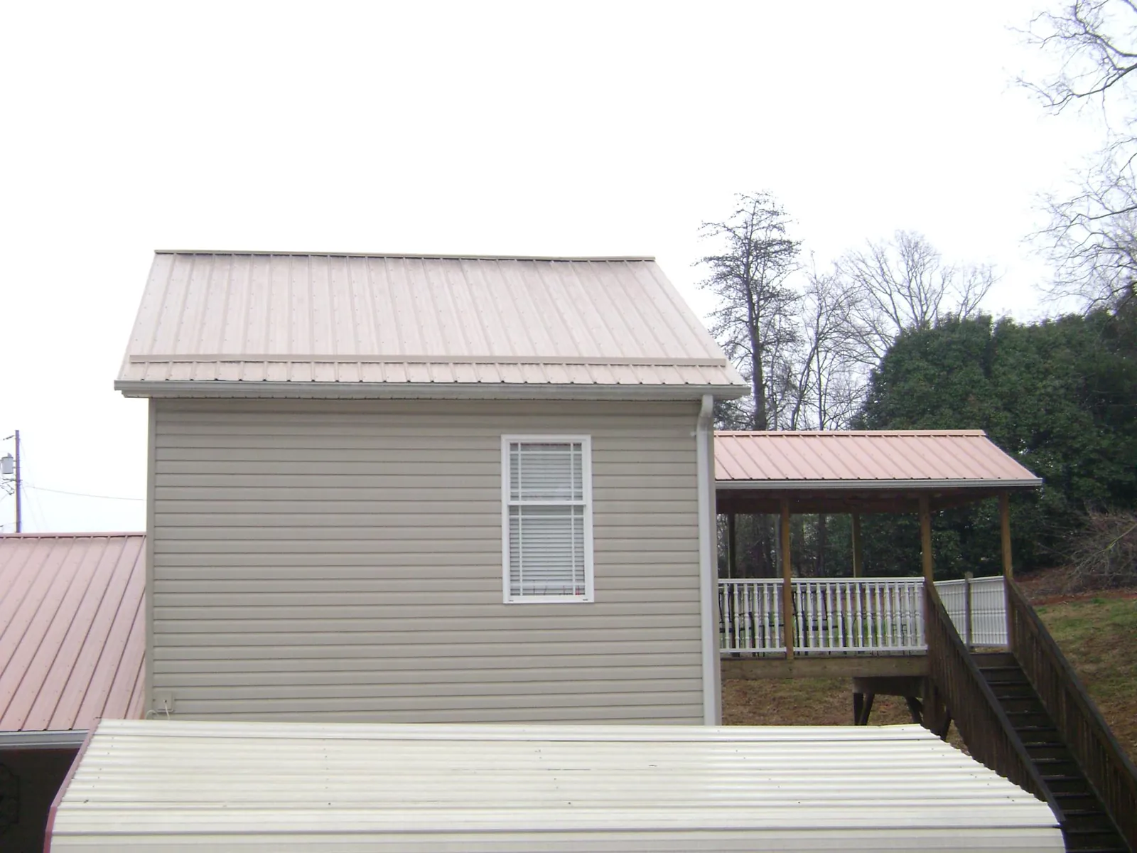 Tan metal roofs on a two story addition and attached porch, from a Roof Replacement job in Columbia